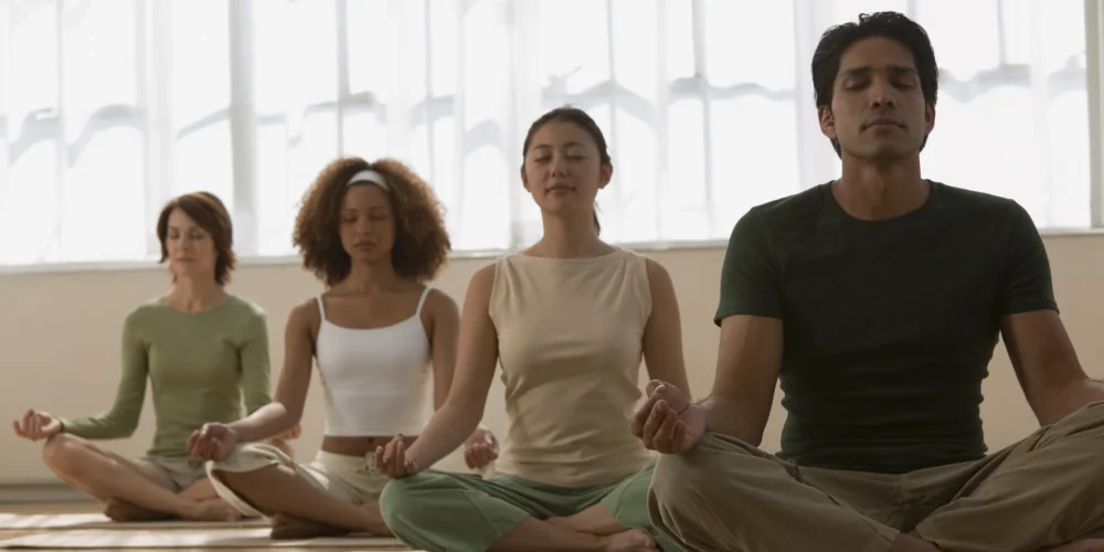Lidé sedící v lotosovém sedu a meditující, praktikující klid a mindfulness